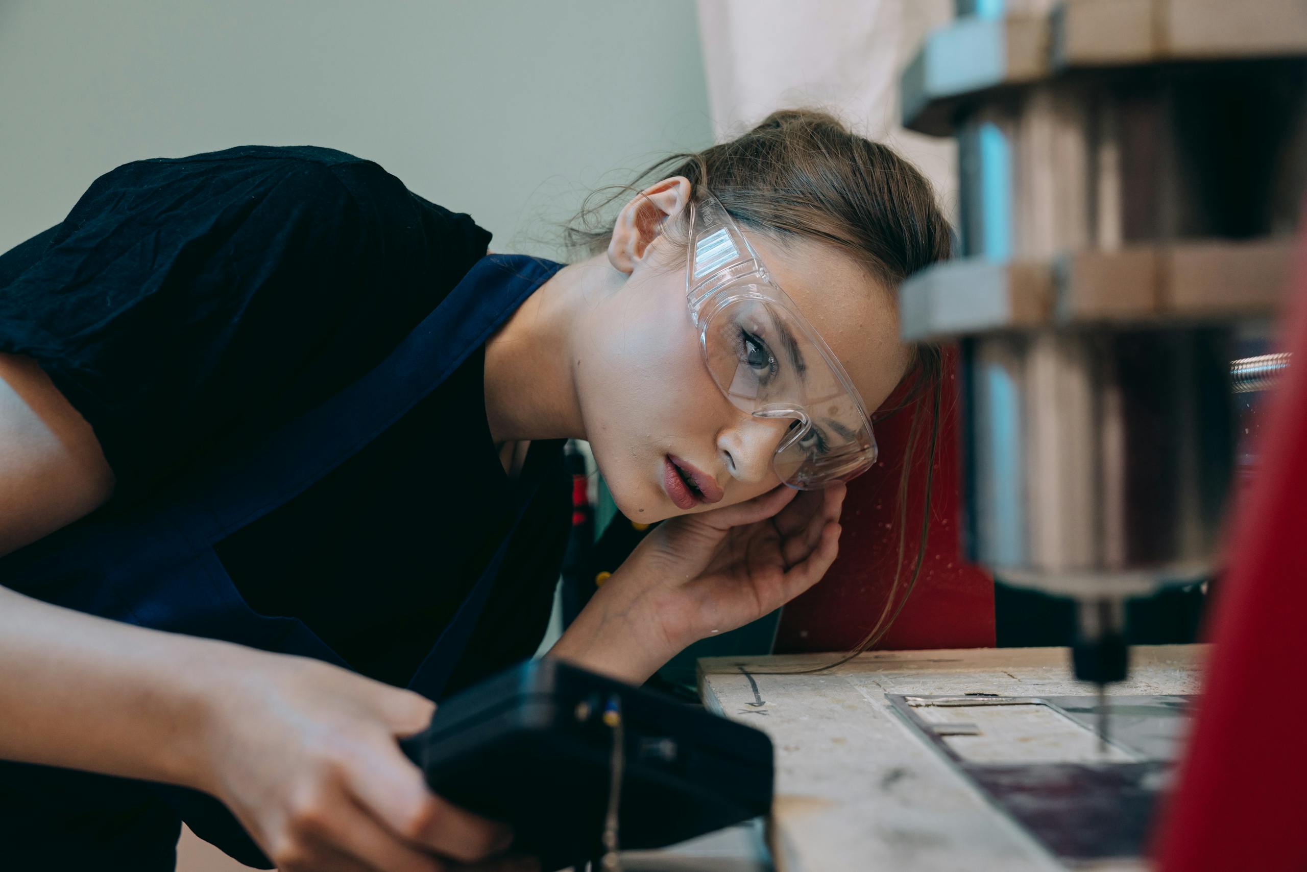 Young woman in workshop wearing goggles, focusing on machinery operation.